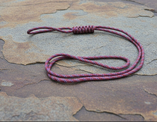 A paracord lanyard with a long loop design, displayed on a stone surface.