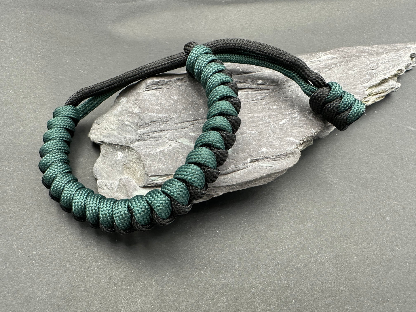 Paracord survival bracelets in a black and Emerald green colour, the item is lightweight comfortable and handmade in a snake knott tactical design U.K.
