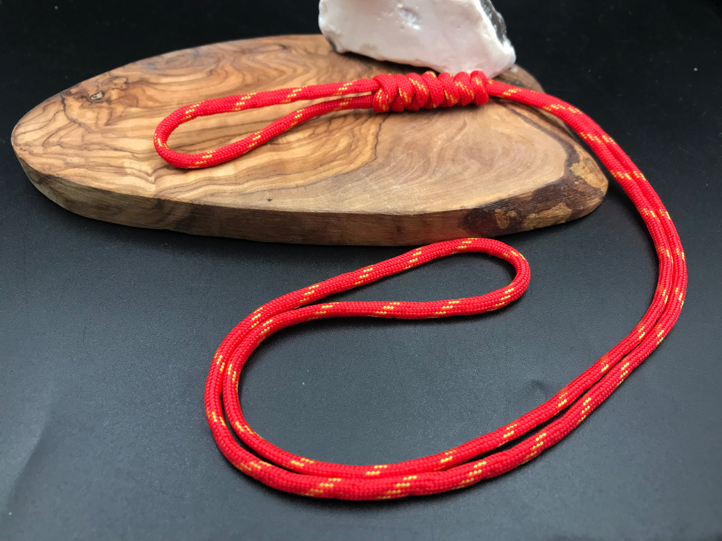 A red with yellow  paracord lanyard with a long loop design, displayed on a wooden surface.