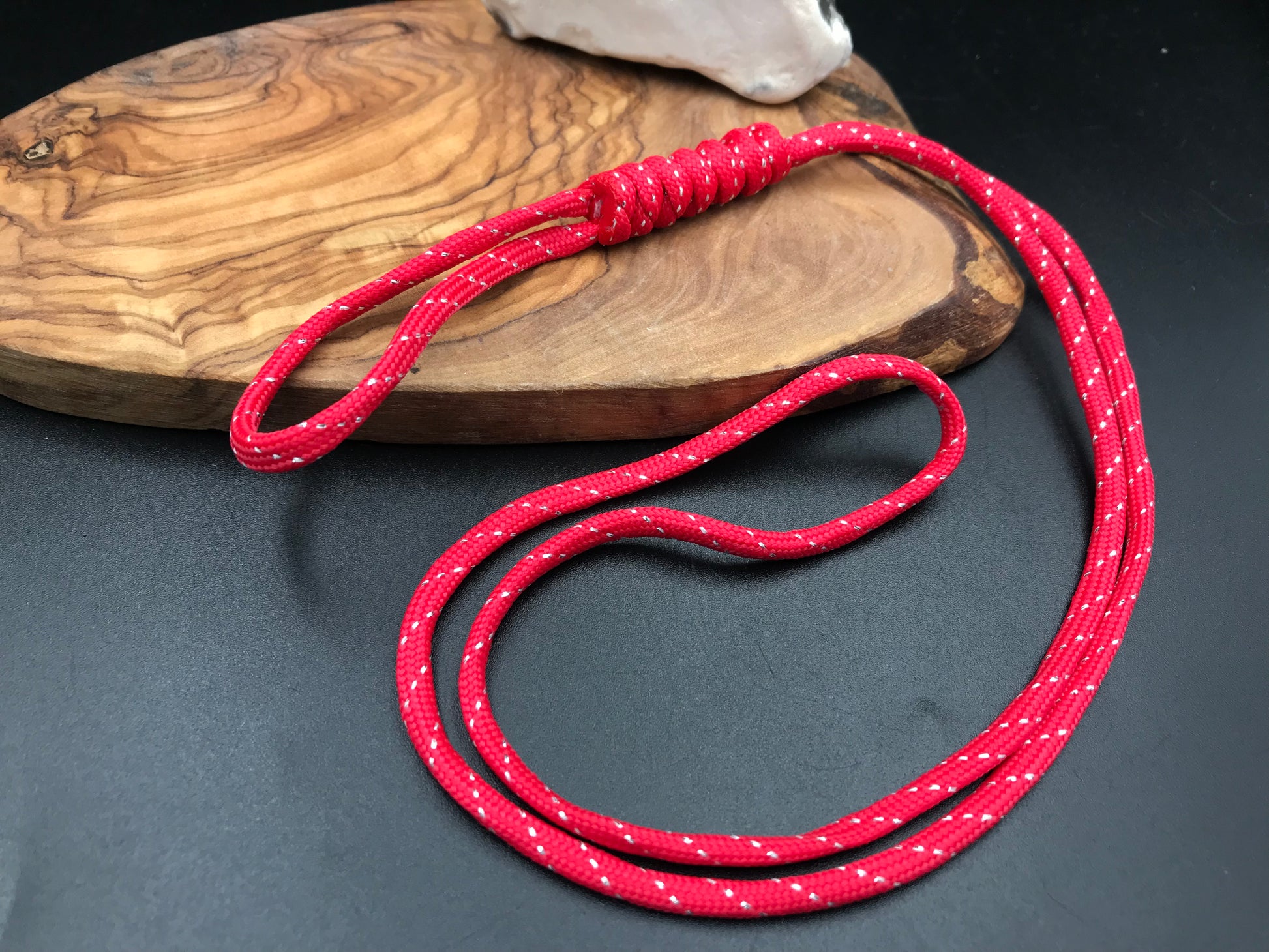 A red  paracord lanyard with a long loop design, displayed on a wooden surface.