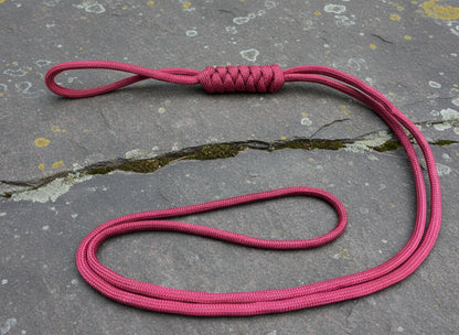 A Burgundy paracord lanyard with a long loop design, displayed on a stone surface.